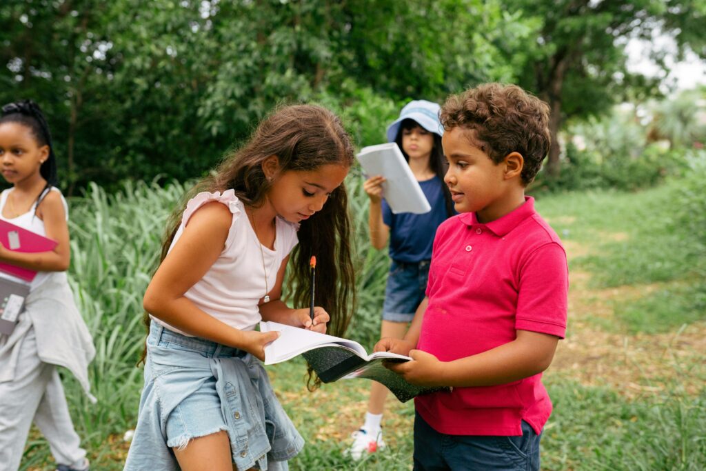 Two children take notes in a field guide outside in nature.